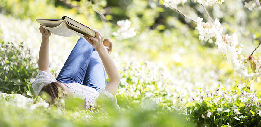 벚꽃 나무 아래 여성이 누워서 책을 보는 사진