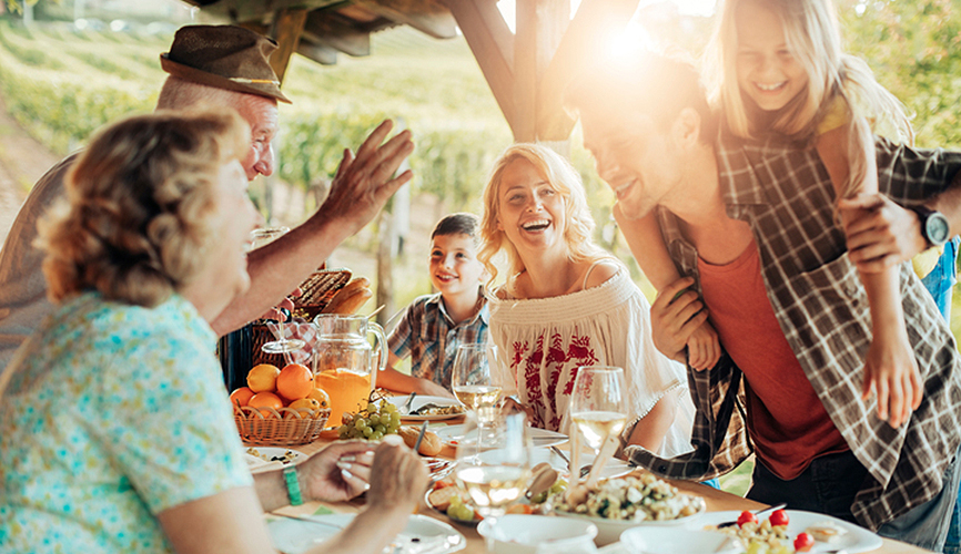 할아버지와 할머니, 아빠, 엄마, 아들, 딸이 과일과 주스, 빵, 식사가 차려진 야외 식탁에서 앉아서 활짝 웃고 있는 사진