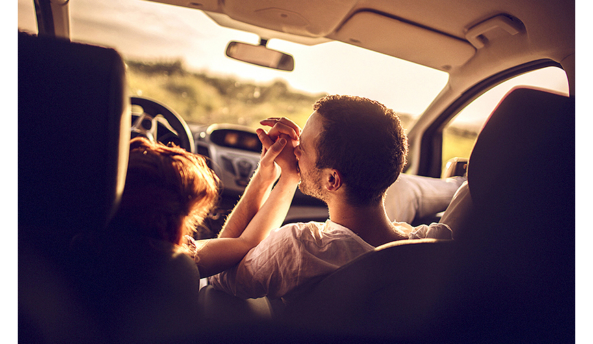 차 안에 앉은 남녀가 서로의 손을 잡고 있으며 남성이 여성의 손 등에 입맞춤을 하고 있는 사진