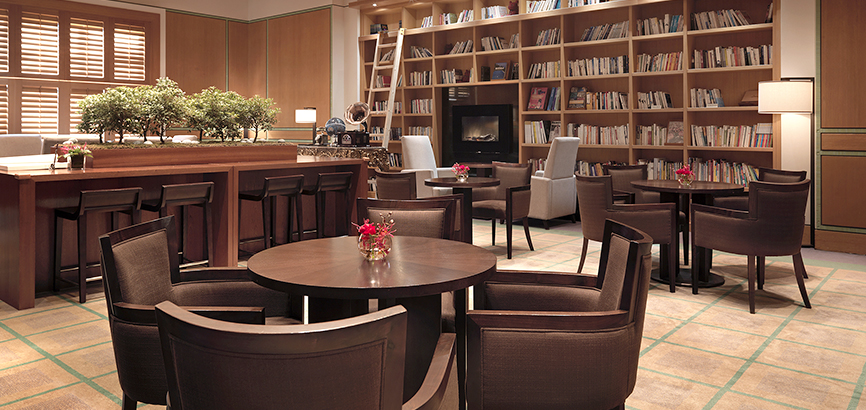 의자가 둘러진 테이블이 여러개 있고 뒷편에는 책이 가득 꽂혀진 높은 책장이 있다.