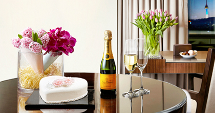 首尔新罗酒店客房的桌子上放着黄牌香槟一瓶，两个香槟杯，水果奶油蛋糕和雪白的花束装点。