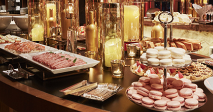 테이블 위에 촛대 장식과 디저트류, 과일이 놓여 있으며, 뒤편으로는 치즈 섹션과 촛대 장식, 창가 야경이 보인다.