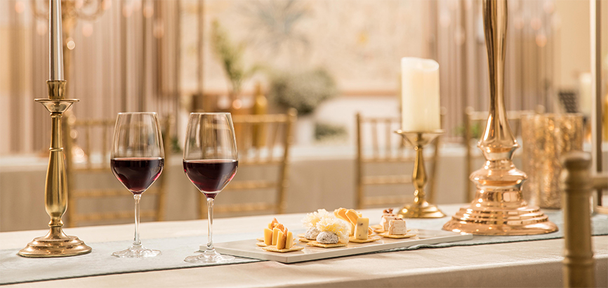 촛대와 초로 장식된 테이블 위 와인이 담긴 잔과 함께 곁들여 먹을 수 있는 음식이 놓여져있다.