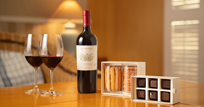 테이블 위 와인이 담겨진 와인 잔2개, 하우스 와인 1병, 쿠키 2종과 초콜렛 6개가 있는 이미지