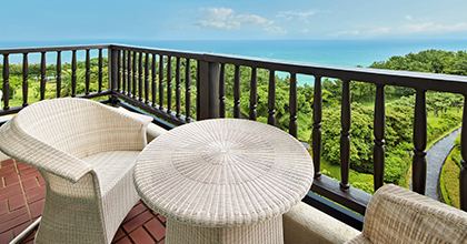 라탄 테이블과 의자가 놓여져 있고 중문 바다와 숨비정원이 보이는 객실 발코니 이미지
