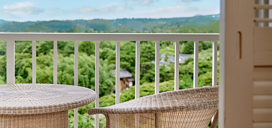 라탄 테이블과 의자가 놓여져 있고 하늘과 산이 보이는 발코니 이미지 