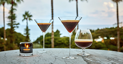 야자수를 배경으로 테이블 위에 커피 칵테일 세 잔과 양초에 불이 켜져있는 이미지.