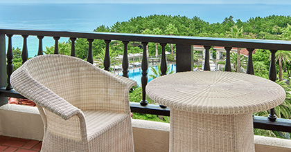 Image of a balcony with a rattan table and chairs overlooking the azure ocean