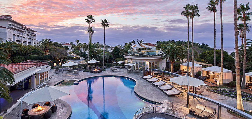 ピンク色に染まった空とヤシの木を背景にした屋外プールの全景画像